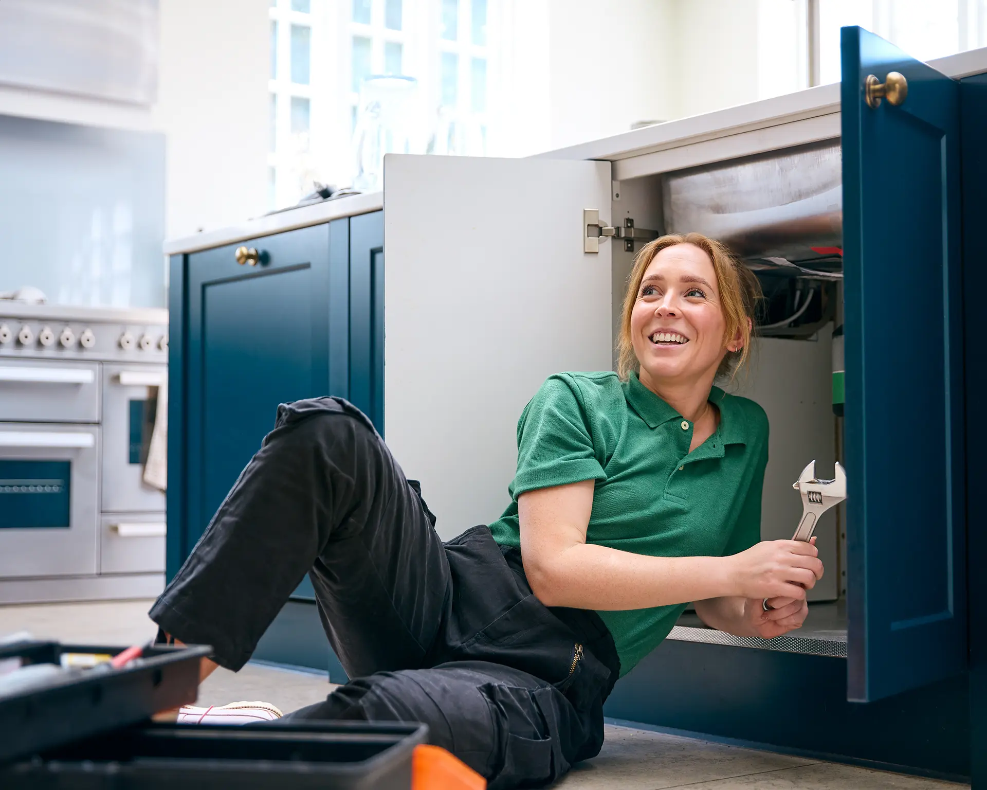 female plumber fixing under sink smiling