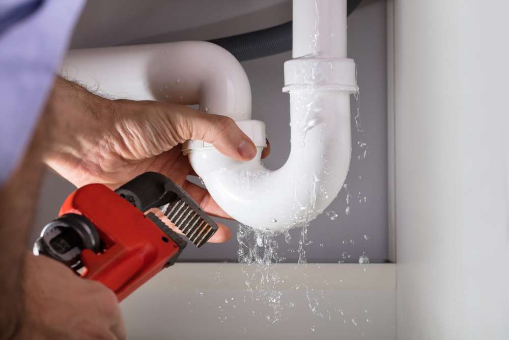 a leaking pipe under a bathroom sink and a plumber trying to fix it with a wrench