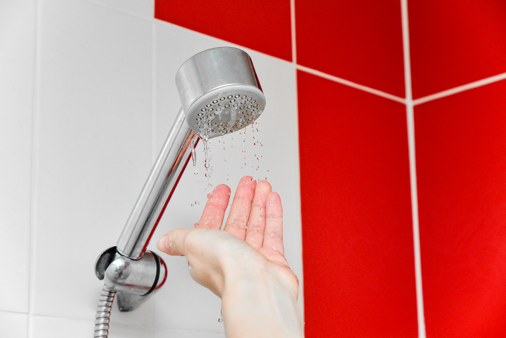 A trickling showerhead and someone reaching their hand up to feel it